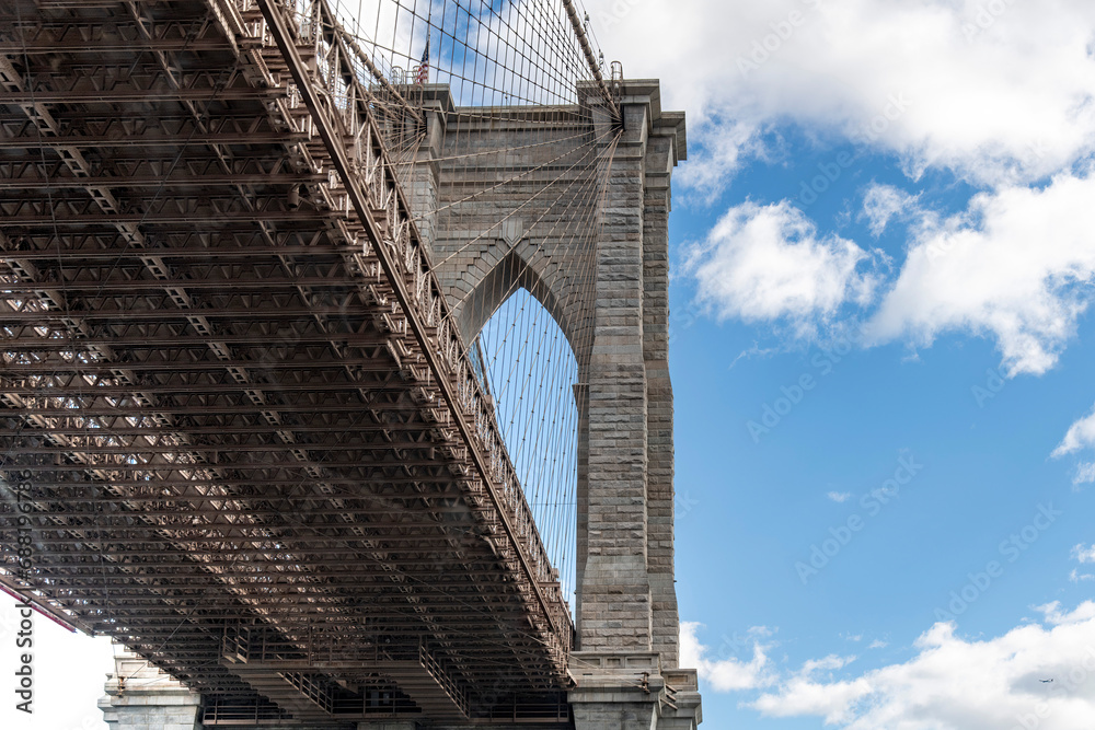 Obraz premium Low angle view of one of the suspension towers of the Brooklyn Bridge, New York City, NY, USA with view of bridge deck against a white clouded blue sky