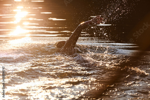 Triathlon athlete swimming on lake in sunrise wearing wetsuit