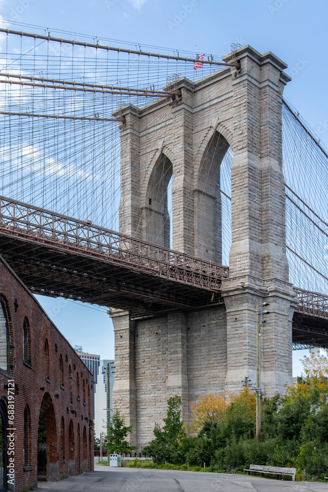 Low angle view of the Brooklyn Bridge, New York City, USA and façade of former Tobacco Warehouse (tobacco customs inspection center) in front along waterfront Brooklyn Bridge Park