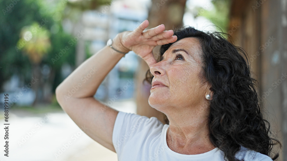 Middle age hispanic woman looking to the sky with serious expression at park Middle age hispanic woman looking to the sky with serious expression at park
