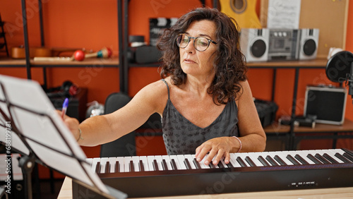 Middle age hispanic woman musician playing piano at music studio