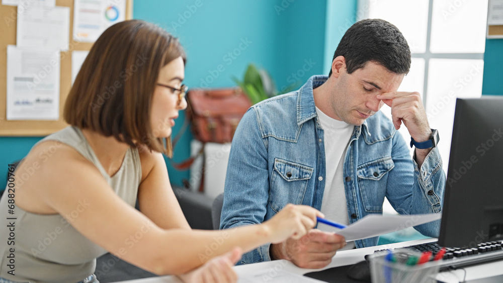 Fototapeta premium Two workers man and woman sitting on table reading document looking upset at the office