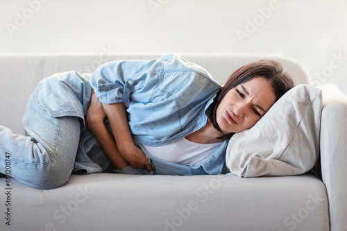 Woman Suffering From Menstrual Cramps Hugging Aching Stomach At Home © Prostock-studio