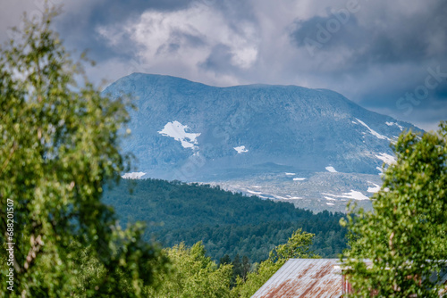 Scenic zoomed view at remote mountain in in Norwegian Mountains range. Blurry trees at foreground at sides of photo. Sweden, Lapland, Joesjo