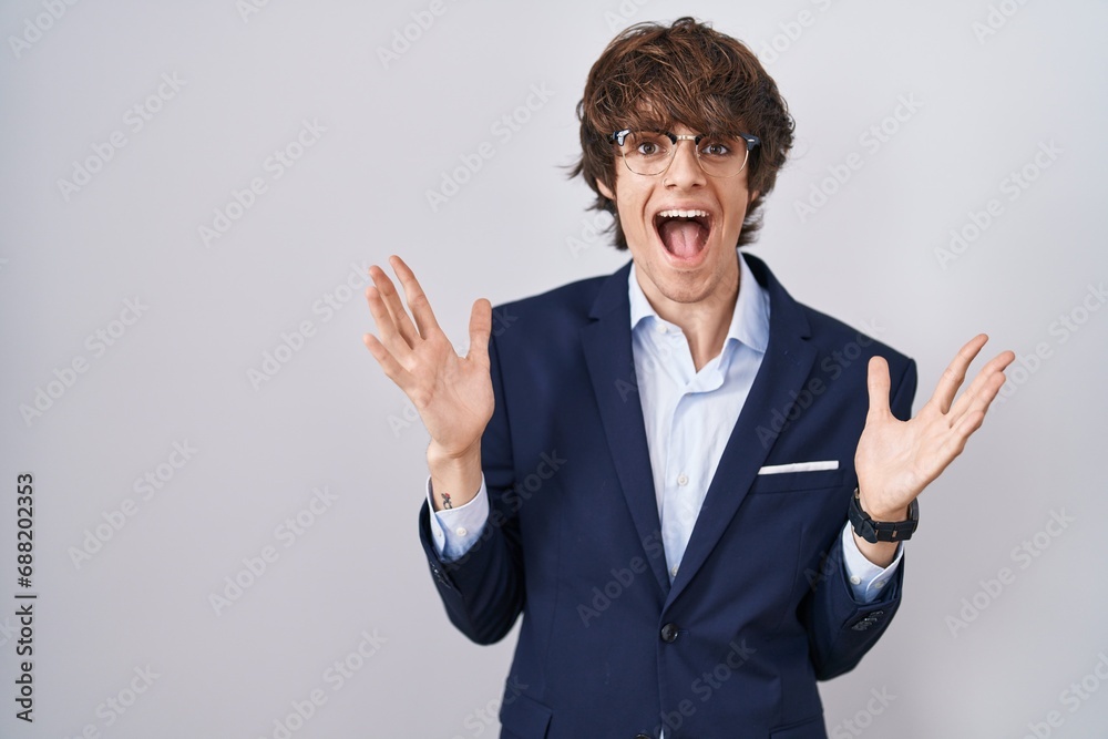 Hispanic business young man wearing glasses celebrating crazy and amazed for success with arms raised and open eyes screaming excited. winner concept