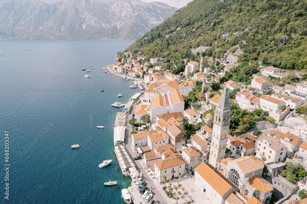 Moored boats off the coast of Perast with the high bell tower of the Church of St. Nicholas among ancient houses. Montenegro. Drone