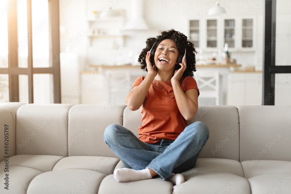 Black woman enjoying music on headphones while sitting on couch at home Black woman enjoying music on headphones while sitting on couch at home