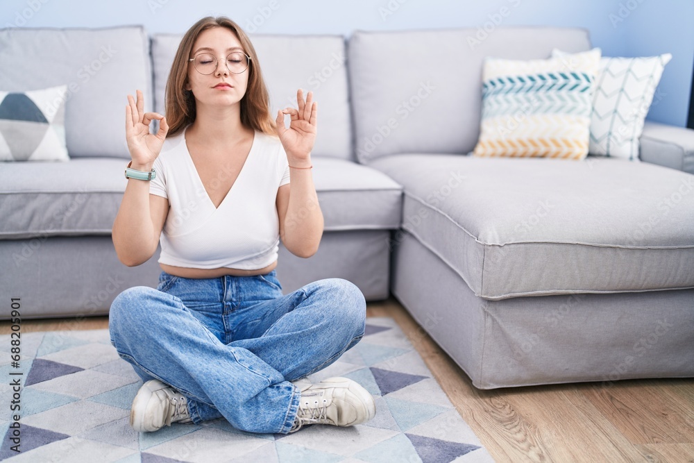Young caucasian woman sitting on the floor at the living room relaxed and smiling with eyes closed doing meditation gesture with fingers. yoga concept. Young caucasian woman sitting on the floor at the living room relaxed and smiling with eyes closed doing meditation gesture with fingers. yoga concept.