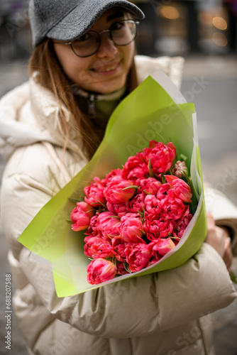 Smiling woman holding a bouquet of pink tulips in a green wrapper, close-up
