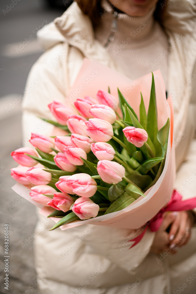 Large bouquet of pink tulips in a pink wrapper is held by a woman