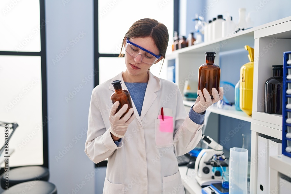 Young blonde woman scientist holding bottles with liquid at laboratory