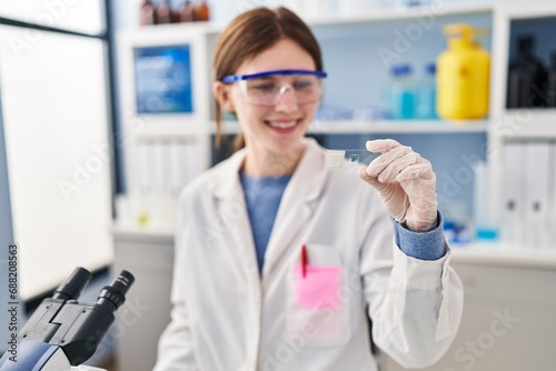 Young blonde woman scientist holding sample smiling at laboratory