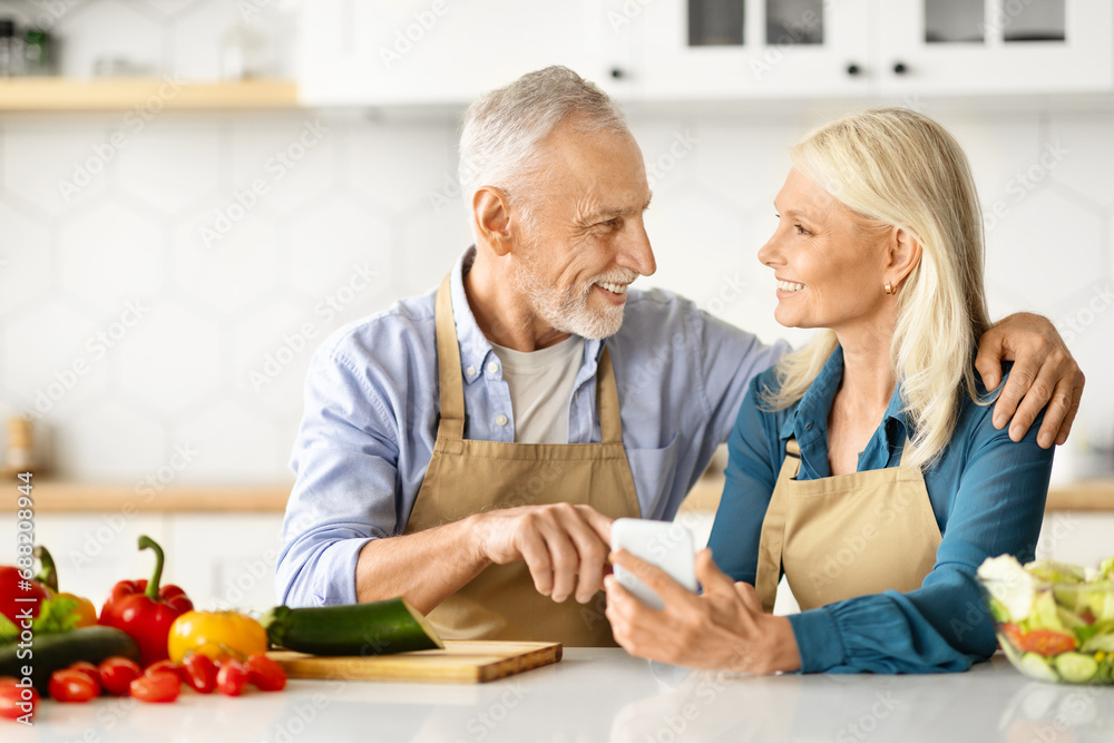 Happy Senior Spouses Ordering Grocery Delivery While Cooking In Kitchen Happy Senior Spouses Ordering Grocery Delivery While Cooking In Kitchen