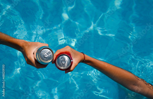 Pool party on summer holiday. Close-up of hands with cans of beer or refreshing drinks in the swimming pool. Selective focus.