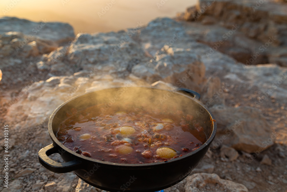 Sizzling shakshuka in a cast iron pan, traditional Middle-Eastern dish, cooked outdoors. Dawn in Mitzpe Ramon. Eggs in tomatoes with sweet bell peppers.