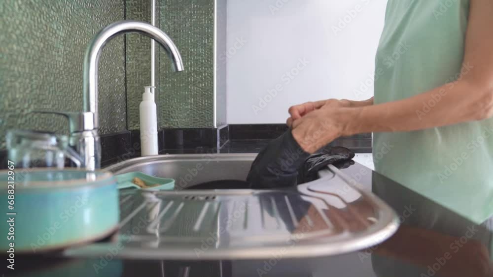 Concept of hand health care, a woman puts black protective gloves on her hands for washing dishes. Concept of hand health care, a woman puts black protective gloves on her hands for washing dishes.