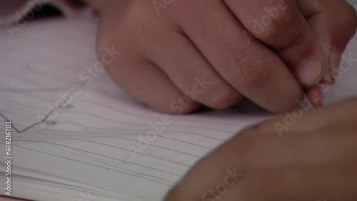 Male Primary Student Making a Line on His Notebook Using a Black Pencil at School. Close Up. photo