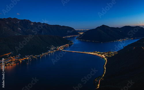 Wide-angle sunset view from the summit of Monte San Salvatore overlooking Lake Lugano Breathtaking panorama of the city, Melide causeway and the Swiss Alps in Ticino, Switzerland - November 2023