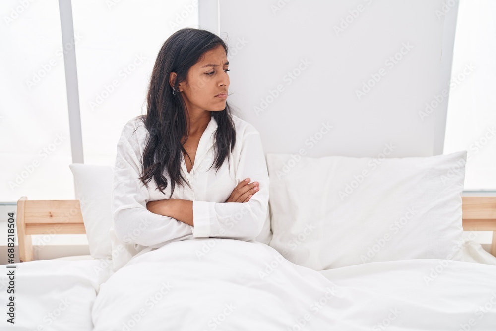 Young beautiful hispanic woman sitting on bed with unhappy expression and arms crossed gesture at bedroom Young beautiful hispanic woman sitting on bed with unhappy expression and arms crossed gesture at bedroom
