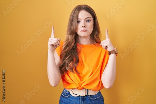 Caucasian woman standing over yellow background pointing up looking sad and upset, indicating direction with fingers, unhappy and depressed. photo