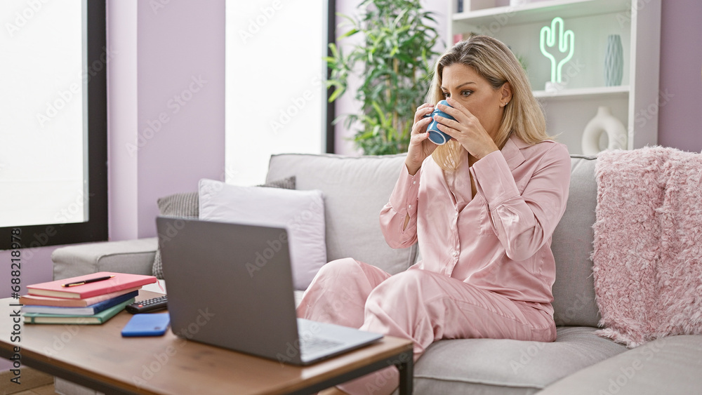 Young blonde woman using laptop drinking coffee at home Young blonde woman using laptop drinking coffee at home