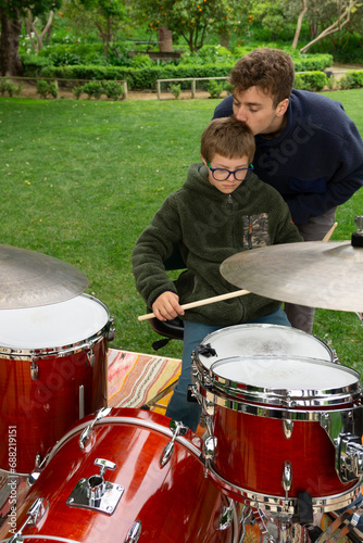 Tender moment: Older brother giving a gentle kiss on his younger brother's forehead while teaching him to play the drums. Down syndrome.