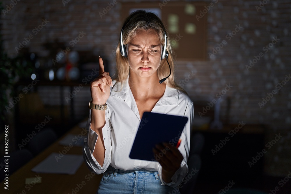 Young blonde woman working at the office at night pointing up looking sad and upset, indicating direction with fingers, unhappy and depressed. - obrazy, fototapety, plakaty 