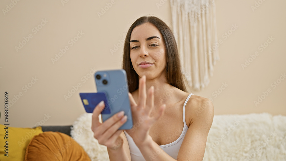 Young beautiful hispanic woman shopping with credit card and touchpad sitting on sofa at home Young beautiful hispanic woman shopping with credit card and touchpad sitting on sofa at home