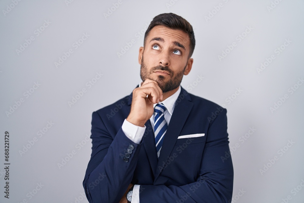 Handsome hispanic man wearing suit and tie with hand on chin thinking about question, pensive expression. smiling with thoughtful face. doubt concept. Handsome hispanic man wearing suit and tie with hand on chin thinking about question, pensive expression. smiling with thoughtful face. doubt concept.