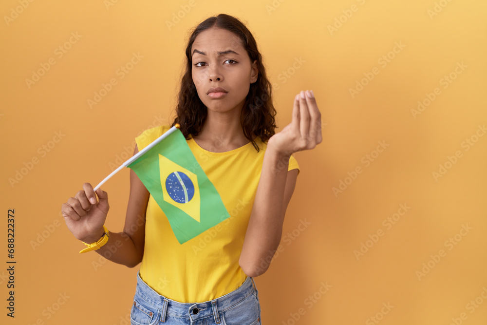 Young hispanic woman holding brazil flag doing italian gesture with hand and fingers confident expression Young hispanic woman holding brazil flag doing italian gesture with hand and fingers confident expression