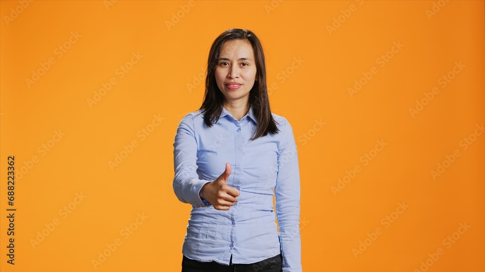 Filipino person showing thumbs up sign on camera, expressing good vibes and positivity over orange background. Young smiling woman giving like in studio, presenting approval gesture. Filipino person showing thumbs up sign on camera, expressing good vibes and positivity over orange background. Young smiling woman giving like in studio, presenting approval gesture.
