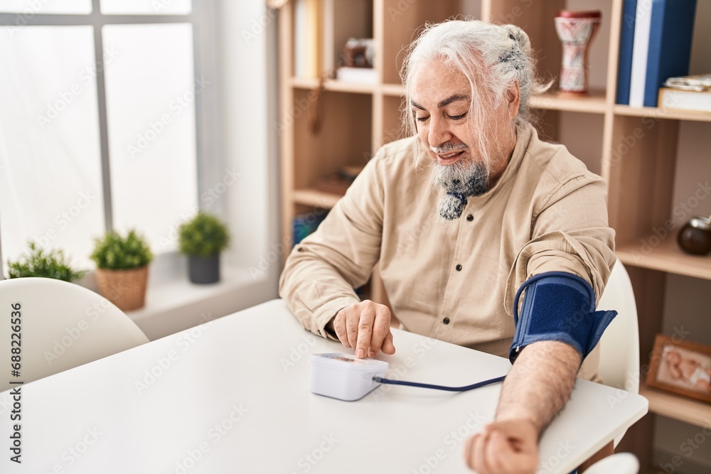 Middle age grey-haired man measuring pulse using tensiometer at home Middle age grey-haired man measuring pulse using tensiometer at home