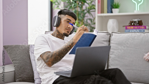 Hardworking young latin man deep in thought, studying with laptop and headphones from the cozy corner of his home living room