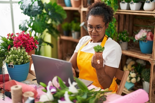 African american woman florist using laptop holding plant at flower shop