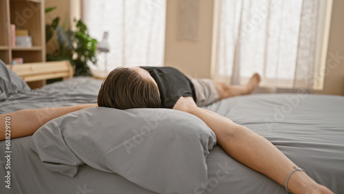 Young hispanic man lying on bed stretching arms at bedroom