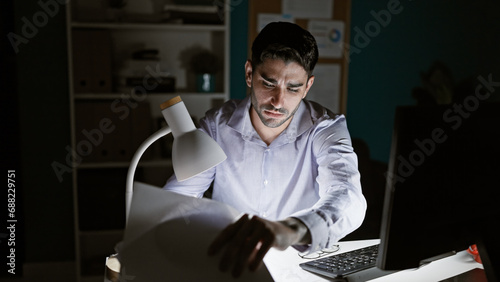 Young hispanic man business worker looking for documents at the office