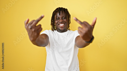 African american man smiling confident doing middle finger gesture over isolated yellow background
