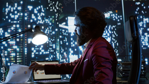 Executive director working at night in his skyscraper office building, examining global investment trends for new career opportunities. Influential businessman with billionaire vision checks reports.