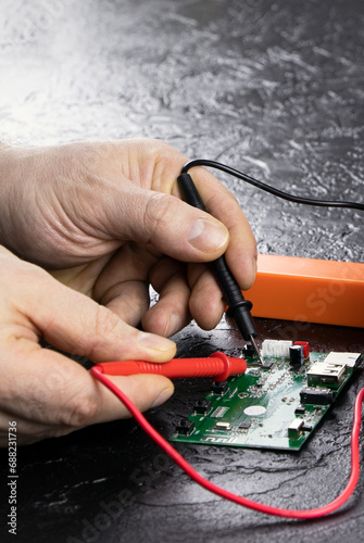 An electrician takes readings from a microcircuit using a multimeter. Measuring instruments. Copy space. Voltage measuring tool. Checking battery voltage. Male hands repairing a microcircuit.