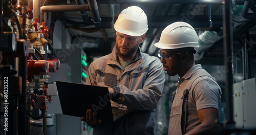 Multiethnic team of technician specialists work together on factory using laptop and tablet computer. Professional engineers discuss industrial manufacturing technology. Concept of heavy industry.