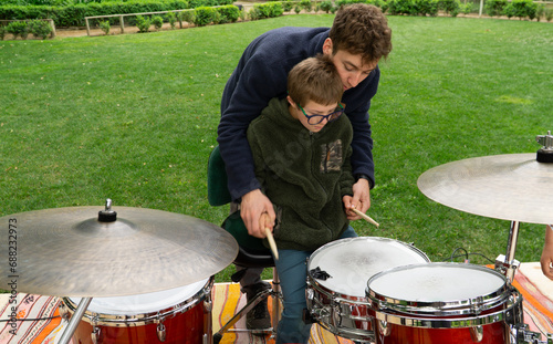 Touching scene of an older brother patiently guiding his younger brother with Down syndrome through a drum lesson, creating a bond through the joy of music.