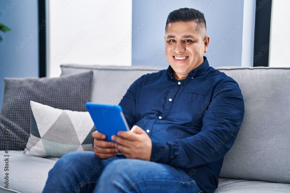 Young latin man using touchpad sitting on sofa at home