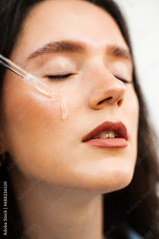 Girl is dropping hyaluronic acid or serum from pipette on face close-up. Young woman is applying moisturizing serum on her face.