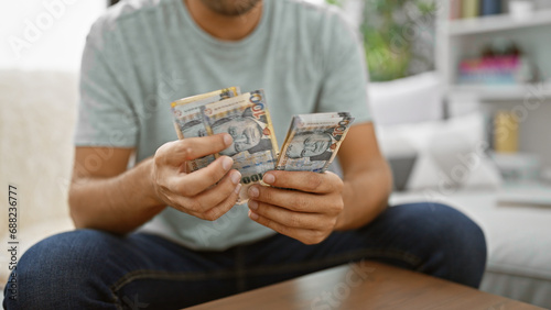 Hispanic young man in living room, sitting on sofa, indulged in counting his wealth - peruvian soles banknotes, mastering home finance. making banking and investment decisions indoors. photo