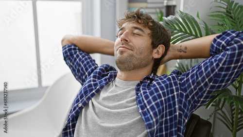 Handsome young blond guy, a happy and confident business worker, relaxed with hands on his head, smiling at success in his elegant office room © Krakenimages.com