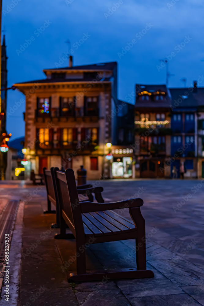 Solitary bench adorned for Christmas, urban bokeh, winter ambiance in Hondarribia square.