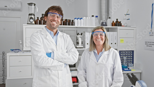 Two confident scientists  man and woman  enjoying work together  joined in relaxed gesture of crossed arms  smiling in the indoor science lab.
