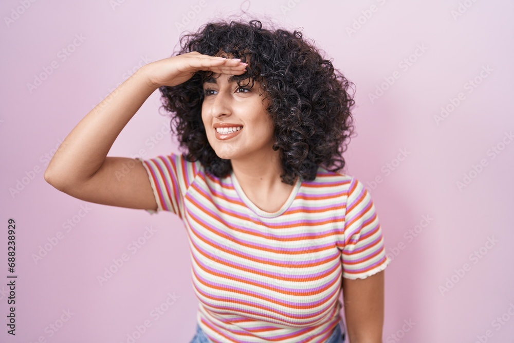 Young middle east woman standing over pink background very happy and smiling looking far away with hand over head. searching concept. Young middle east woman standing over pink background very happy and smiling looking far away with hand over head. searching concept.