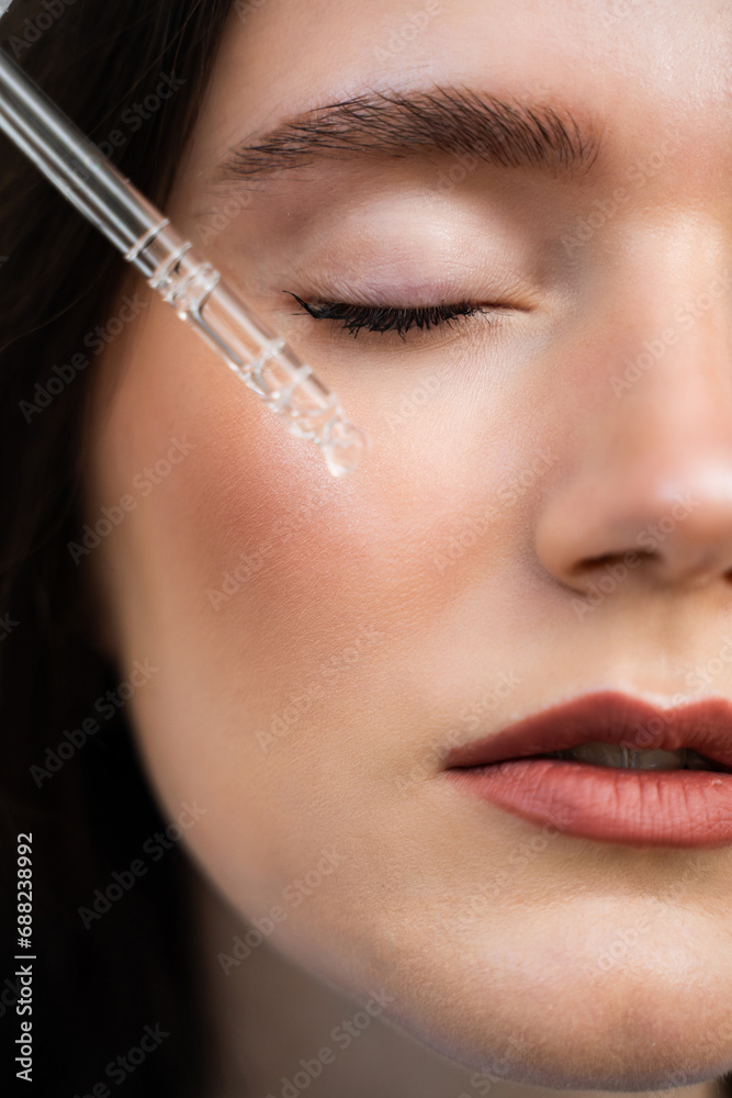 Girl is applying hyaluronic serum with pipette on face. Young woman with acid dropper is applying drops of acid on her skin.