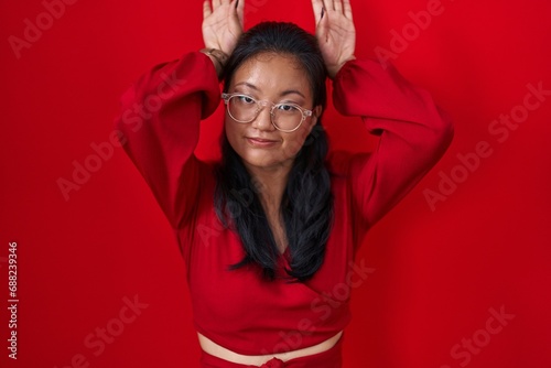 Asian young woman standing over red background doing bunny ears gesture with hands palms looking cynical and skeptical. easter rabbit concept. photo